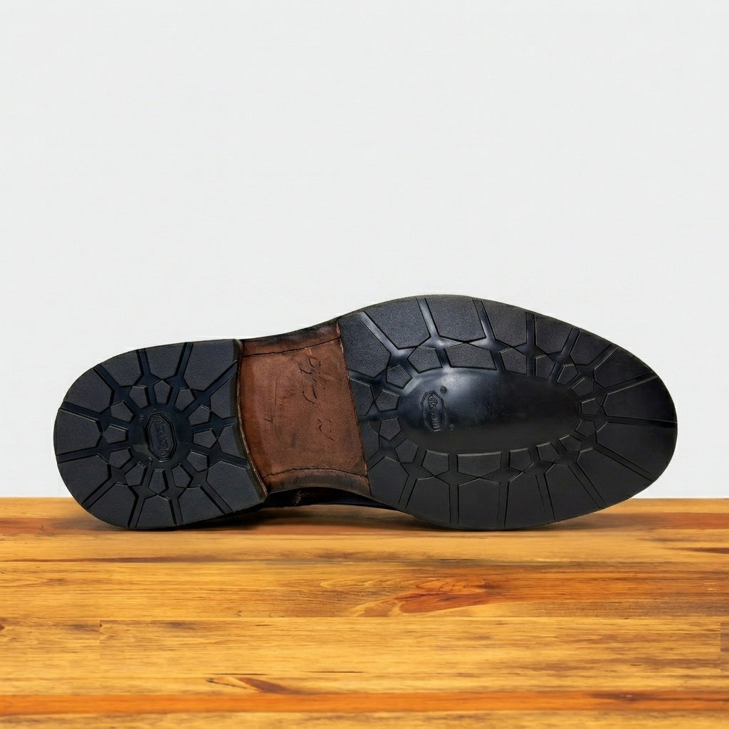 Close-up of a Dark Brown leather shoe sole on a wooden surface.