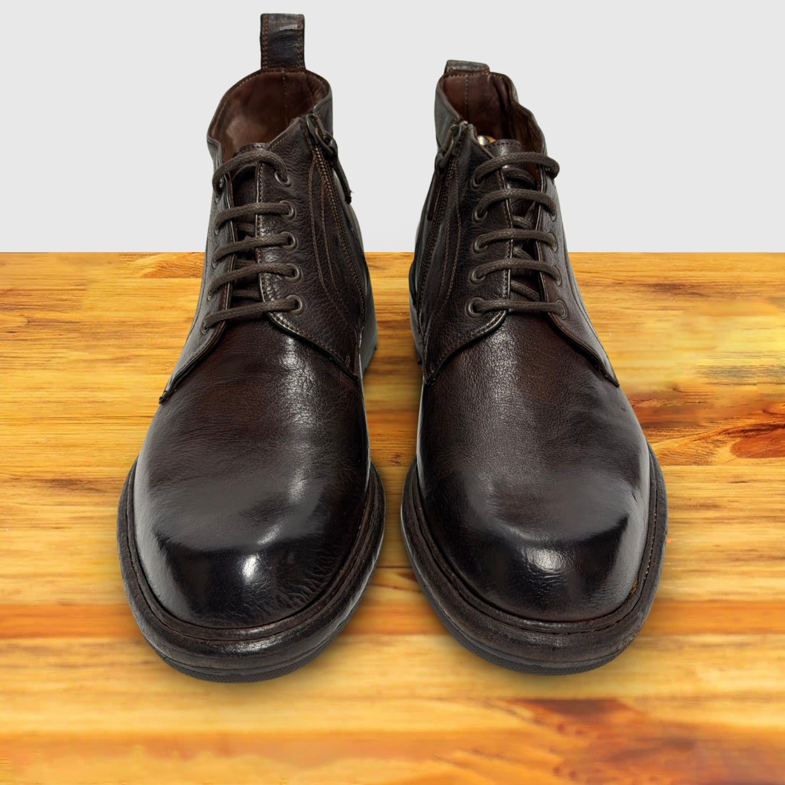 Pair of dark brown leather boots on a wooden surface with a light gray background