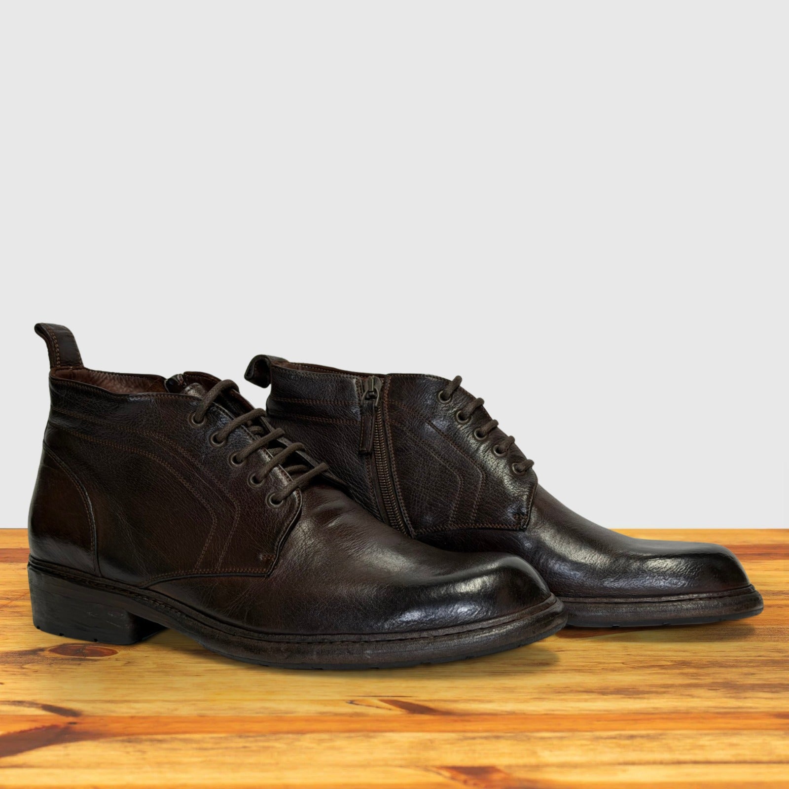 Pair of dark brown leather boots on a wooden surface with a light gray background