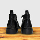Pair of black leather boots on a wooden surface with a light gray background