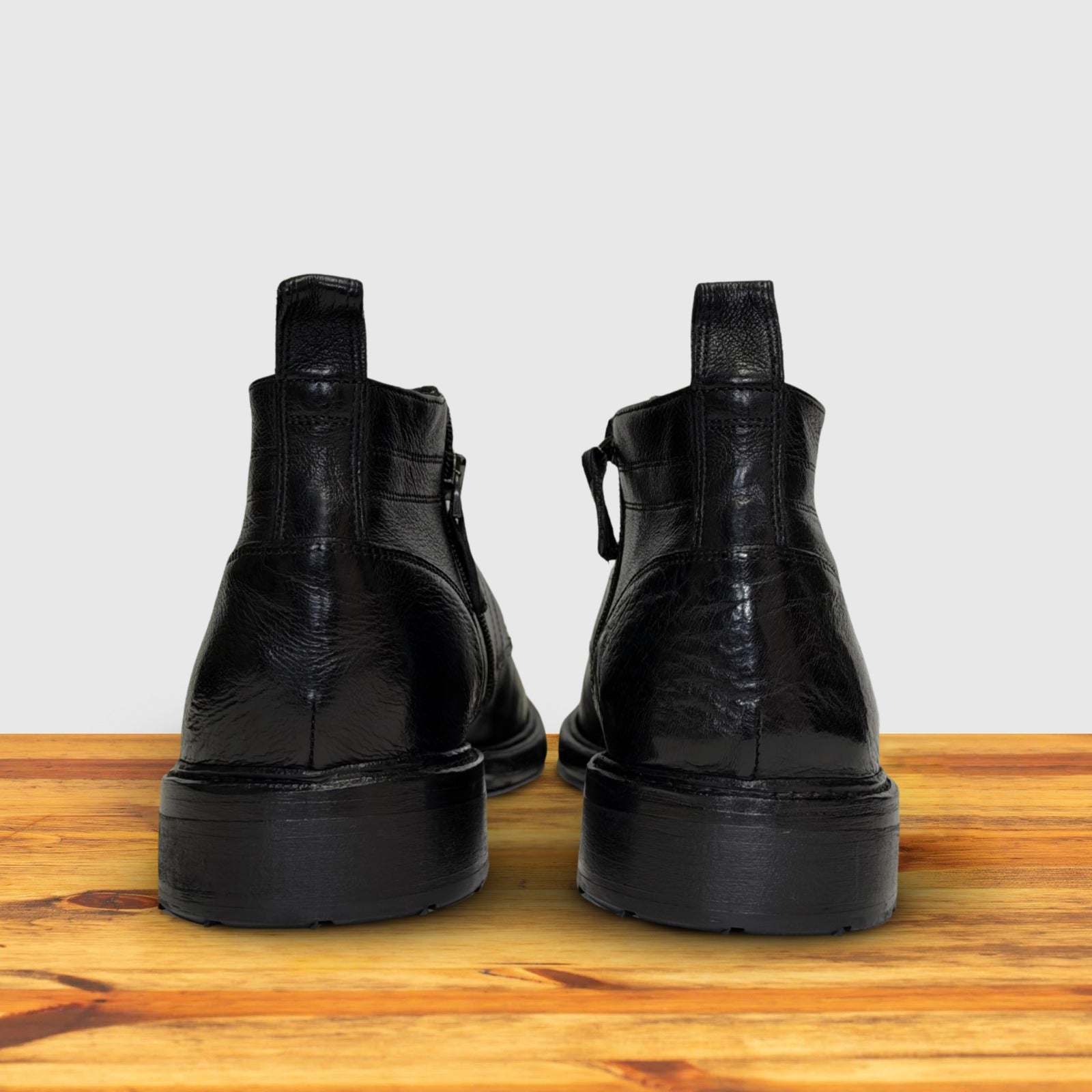 Pair of black leather boots on a wooden surface with a light gray background