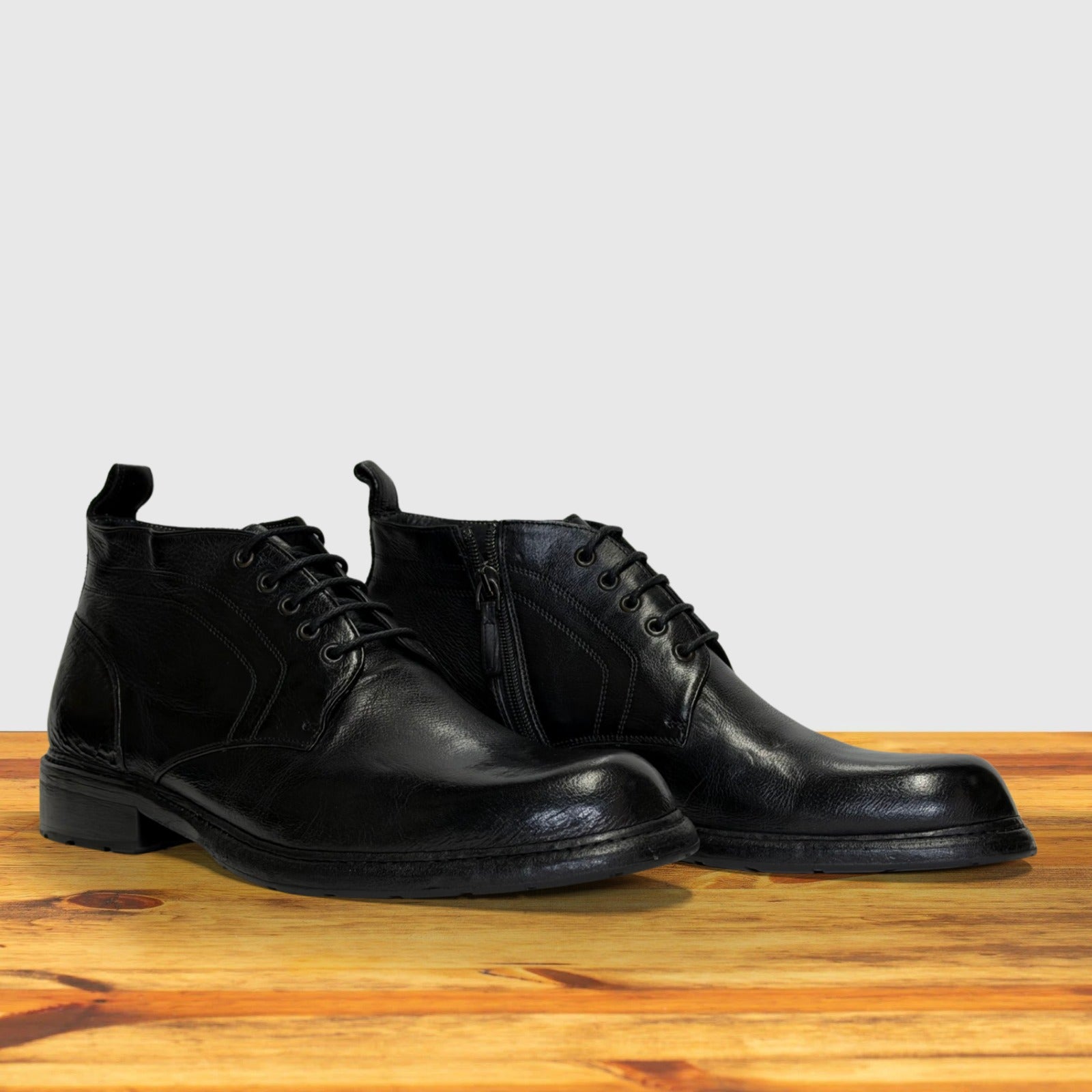 Pair of black leather boots on a wooden surface with a light gray background