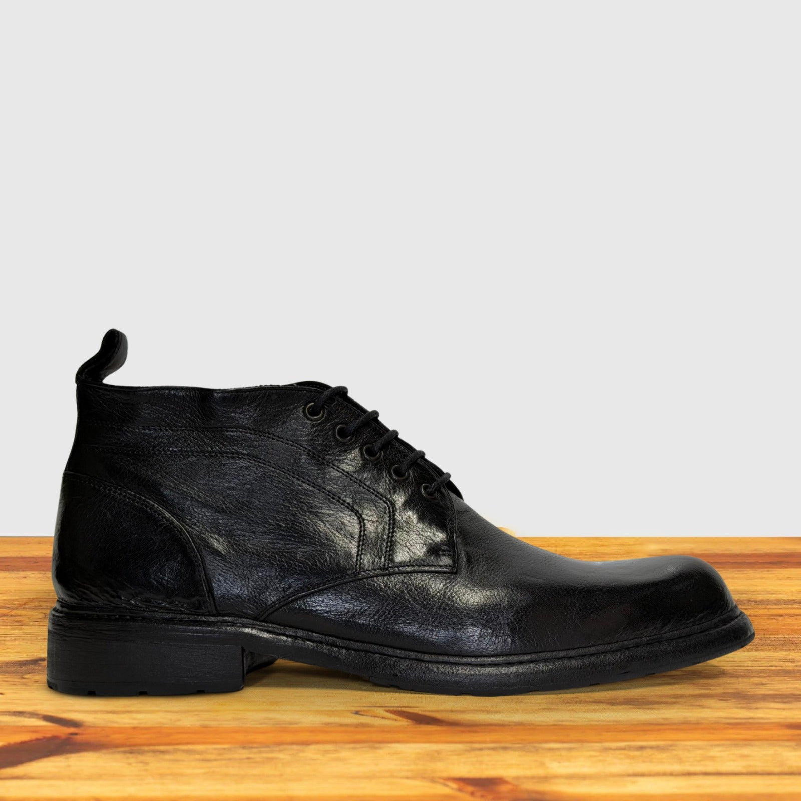 Black leather boot on a wooden surface with a light gray background