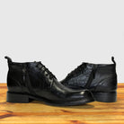 Pair of black leather boots on a wooden surface with a light gray background