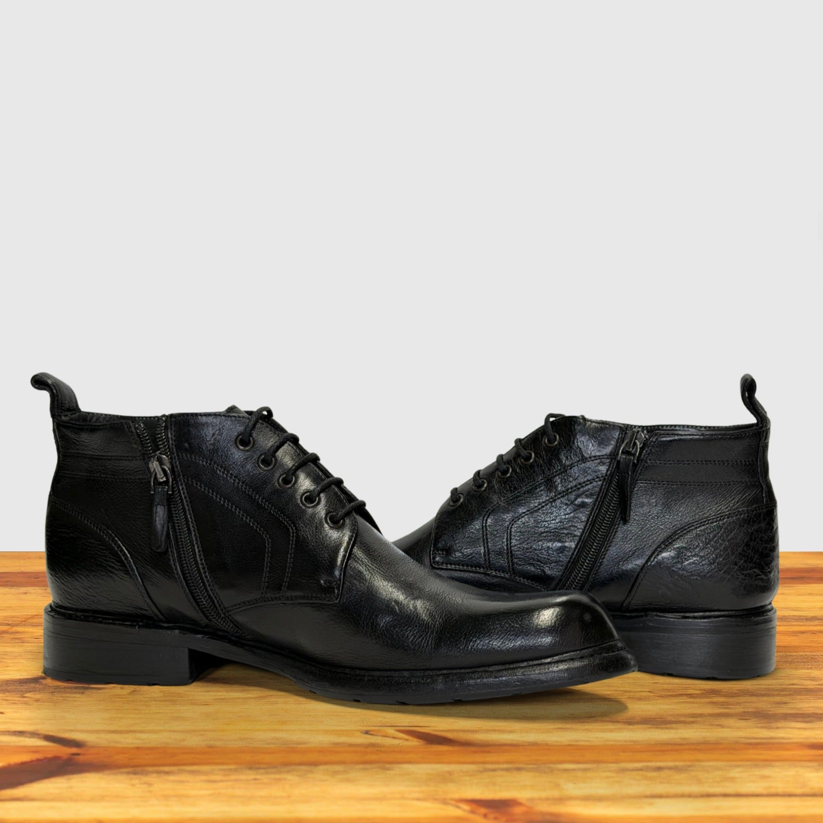 Pair of black leather boots on a wooden surface with a light gray background