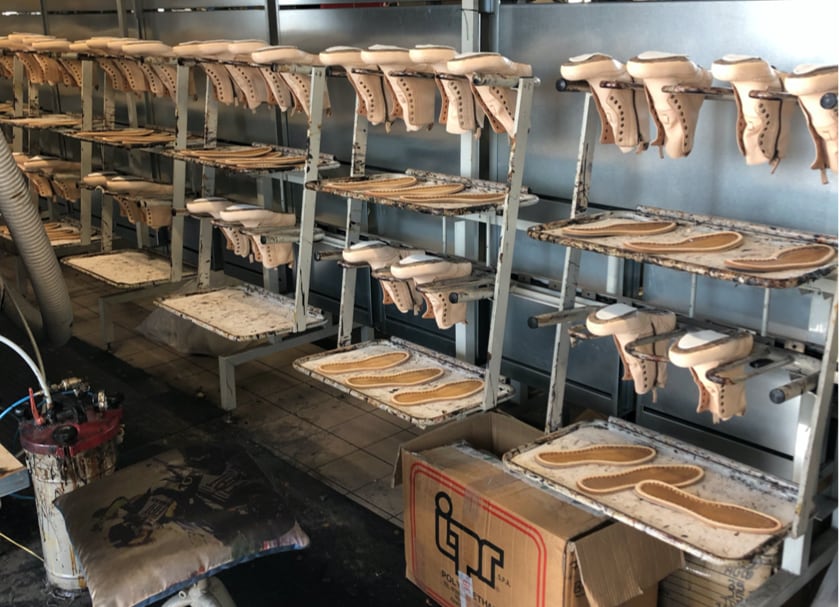 Italian leather shoe uppers and insoles on factory racks during the sole cementing process at the Calzoleria Toscana handcrafted shoe factory in Italy