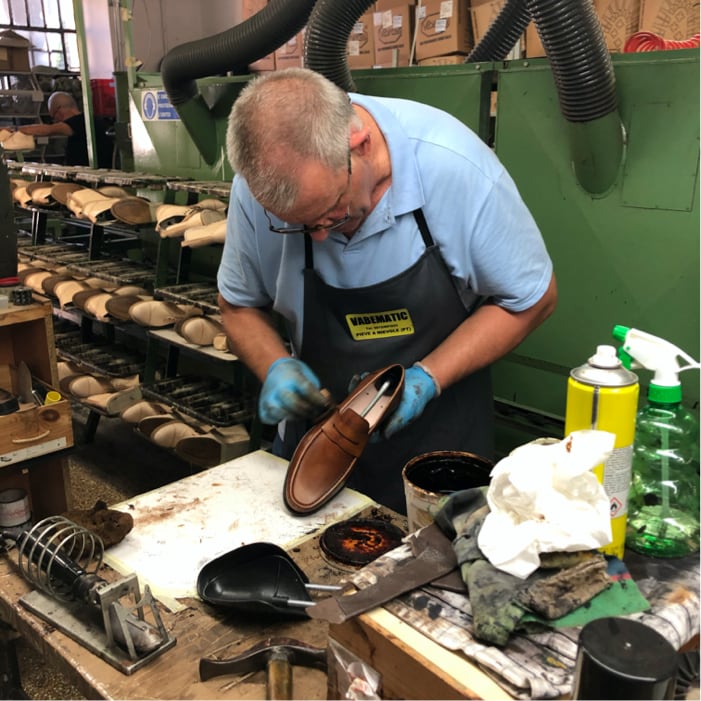 Senior Italian cobbler hand-finishing a tan leather loafer at the Calzoleria Toscana factory workbench