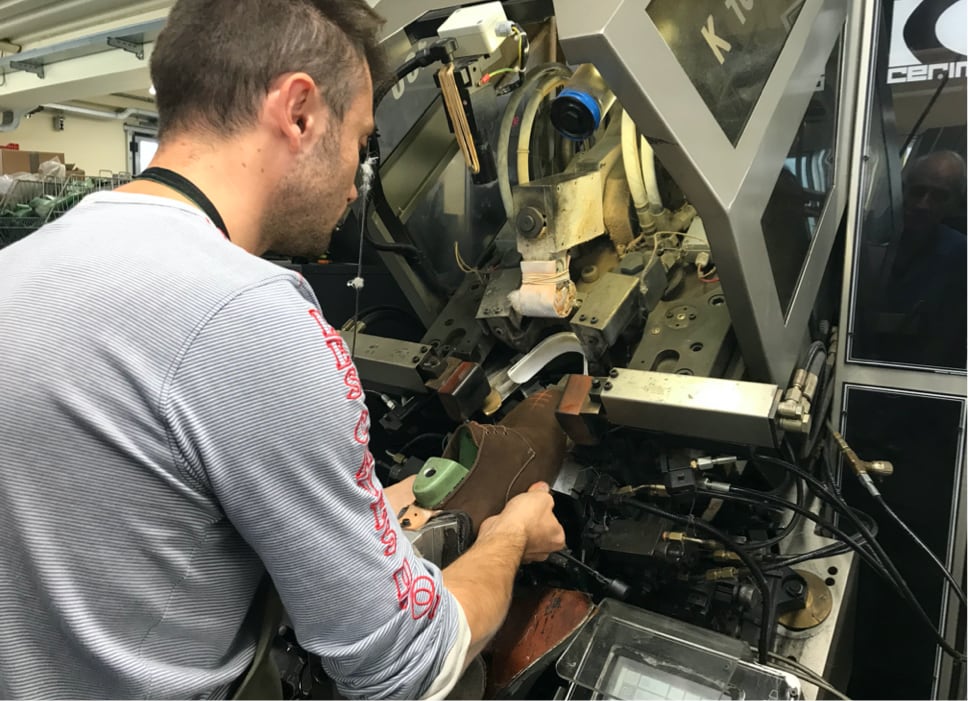 Italian craftsman operating a toe lasting machine to shape leather shoe uppers at the Calzoleria Toscana factory in Italy
