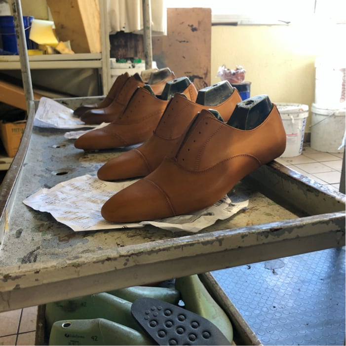 Tan Italian leather monk strap shoes on wooden lasts resting on a factory workbench during handcrafted production at Calzoleria Toscana