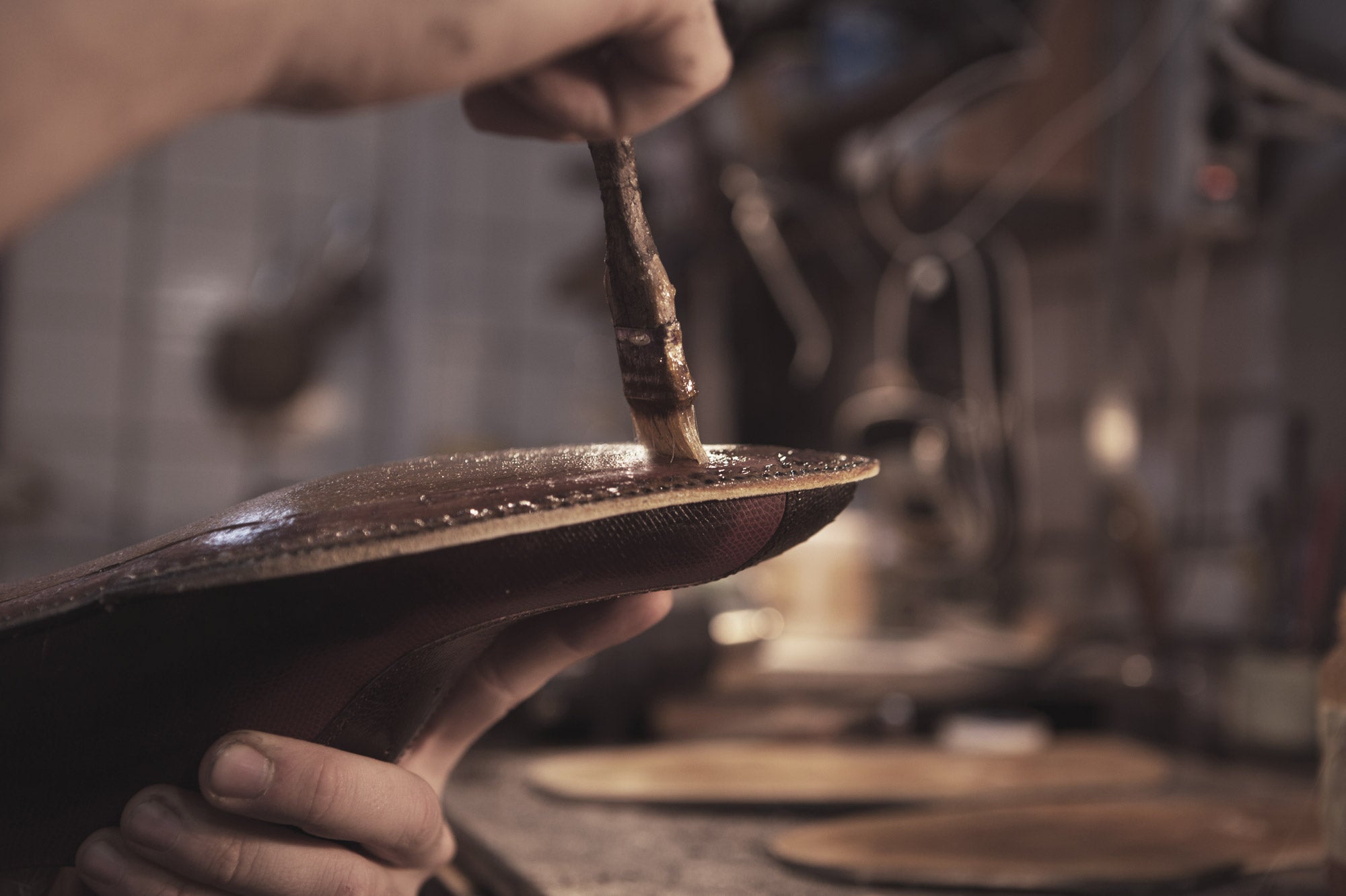 Italian artisan hand-applying glue to a leather shoe sole — traditional Calzoleria Toscana shoemaking technique