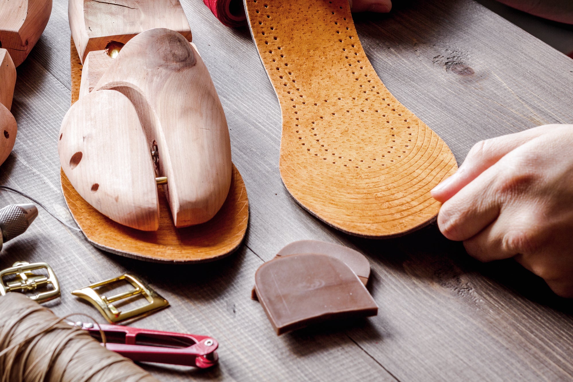 Italian shoemaker's workbench with a wooden shoe last, perforated leather insole, heel counter, gold buckles and waxed thread — handcrafted shoe components used in Calzoleria Toscana men's dress shoes made in Italy