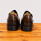 A pair of chestnut leather lace-up shoes shown from the back, resting on a wooden surface against a plain light background.