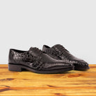 A Pair of Brown crocodile shoe on a wooden surface with a light gray background