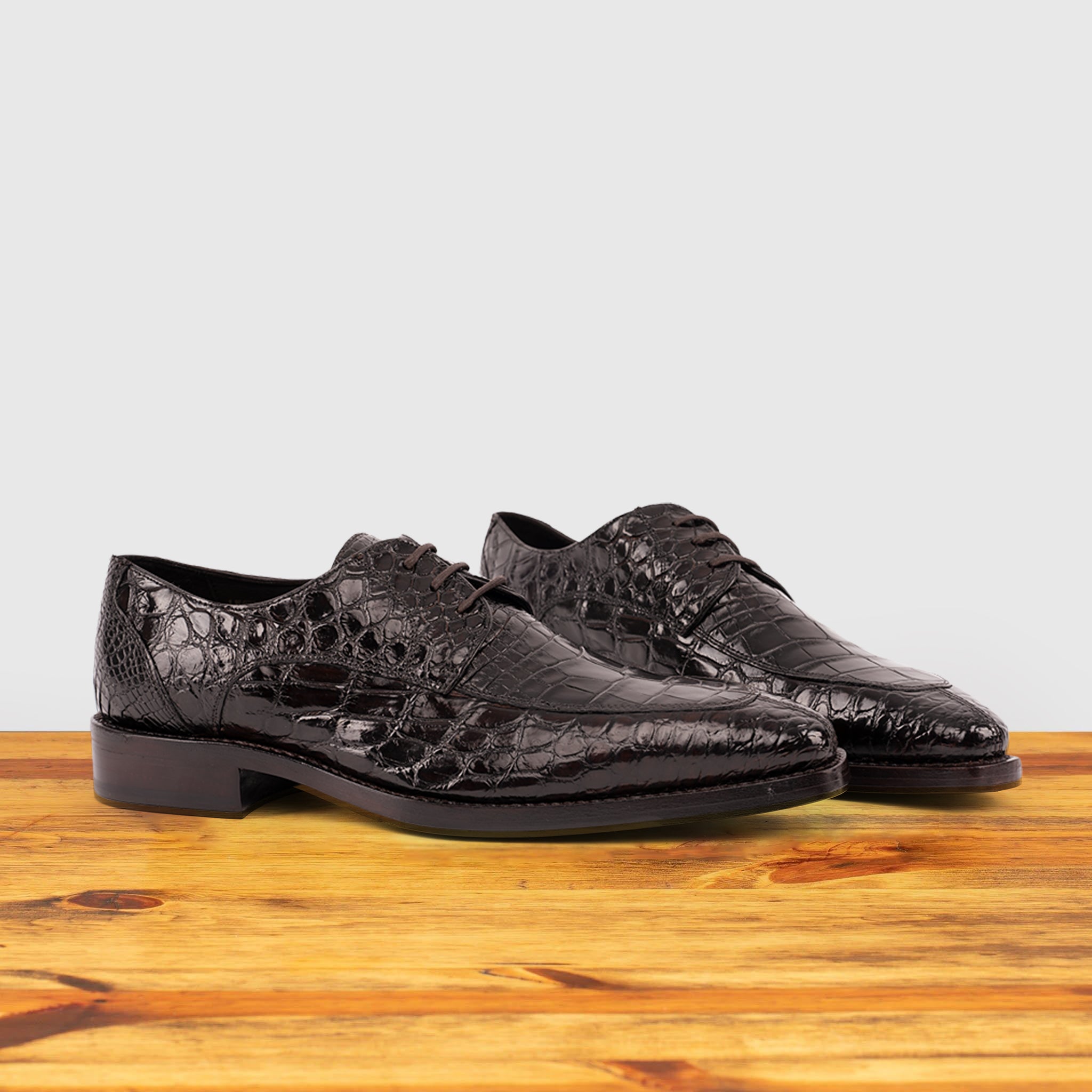 A Pair of Brown crocodile shoe on a wooden surface with a light gray background