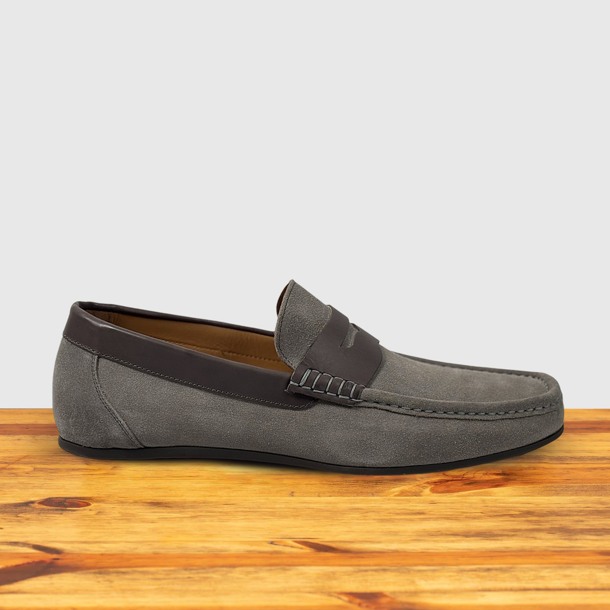  A suede penny loafer with a  strap, displayed on a wooden surface.