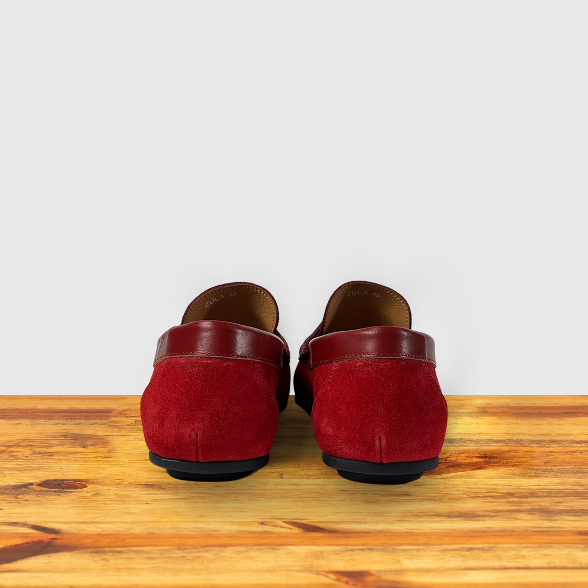 Red loafer shoe on a wooden surface with a light gray background