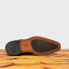 Outsole of Black leather boot on a wooden surface with a gray background