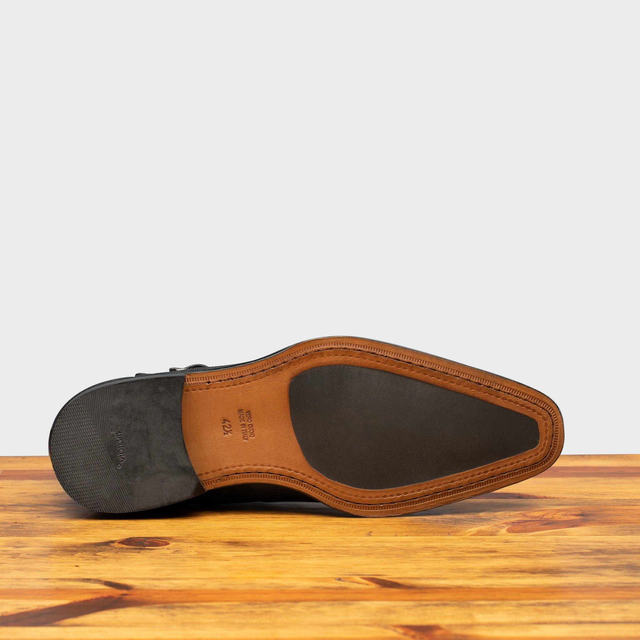 Outsole of Black leather boot on a wooden surface with a gray background