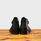 Back view of Black leather boot on a wooden surface with a gray background