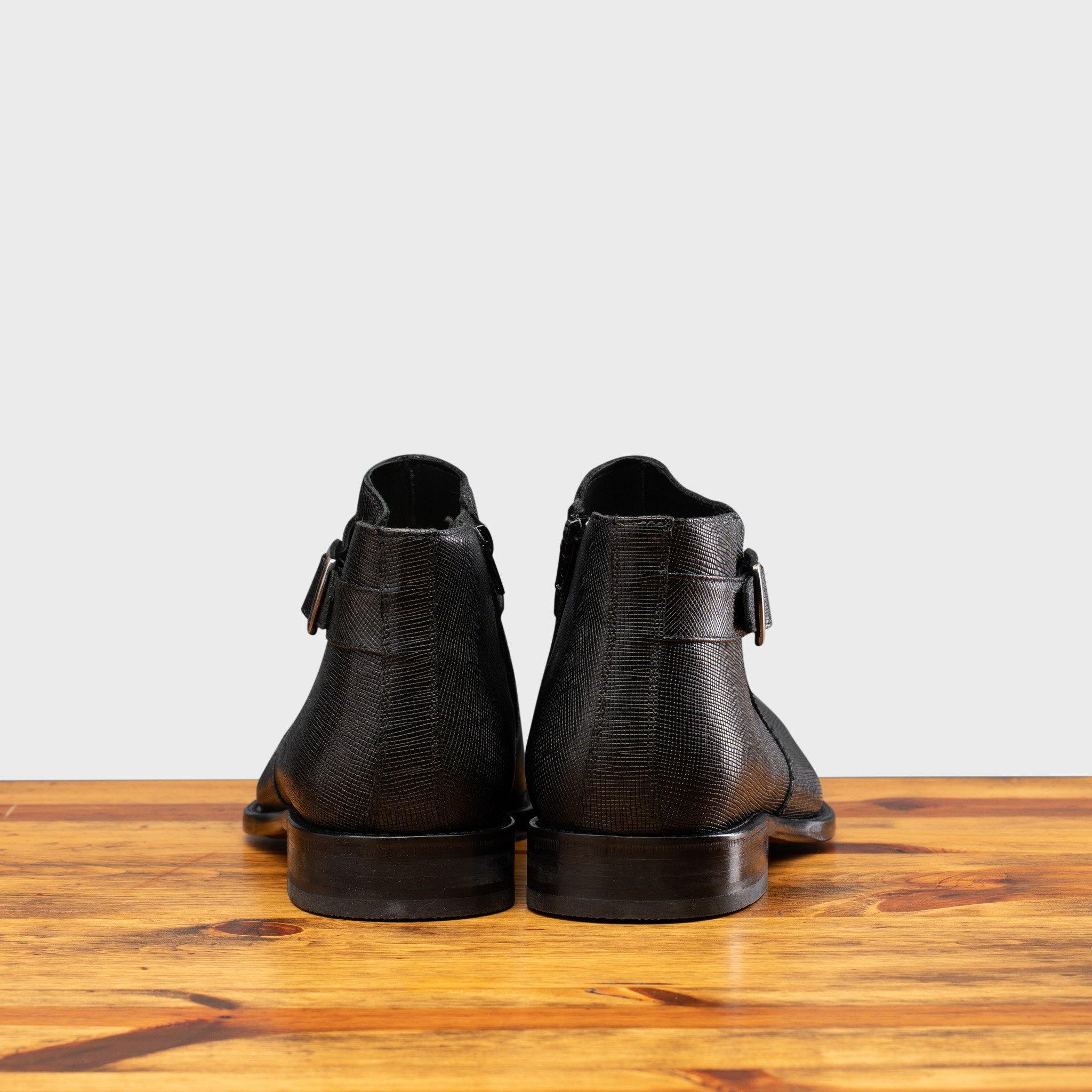 Back view of Black leather boot on a wooden surface with a gray background