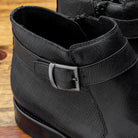 Close-up of Black leather boots on a wooden surface with a gray background