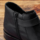 Close-up of Black leather boot on a wooden surface with a gray background