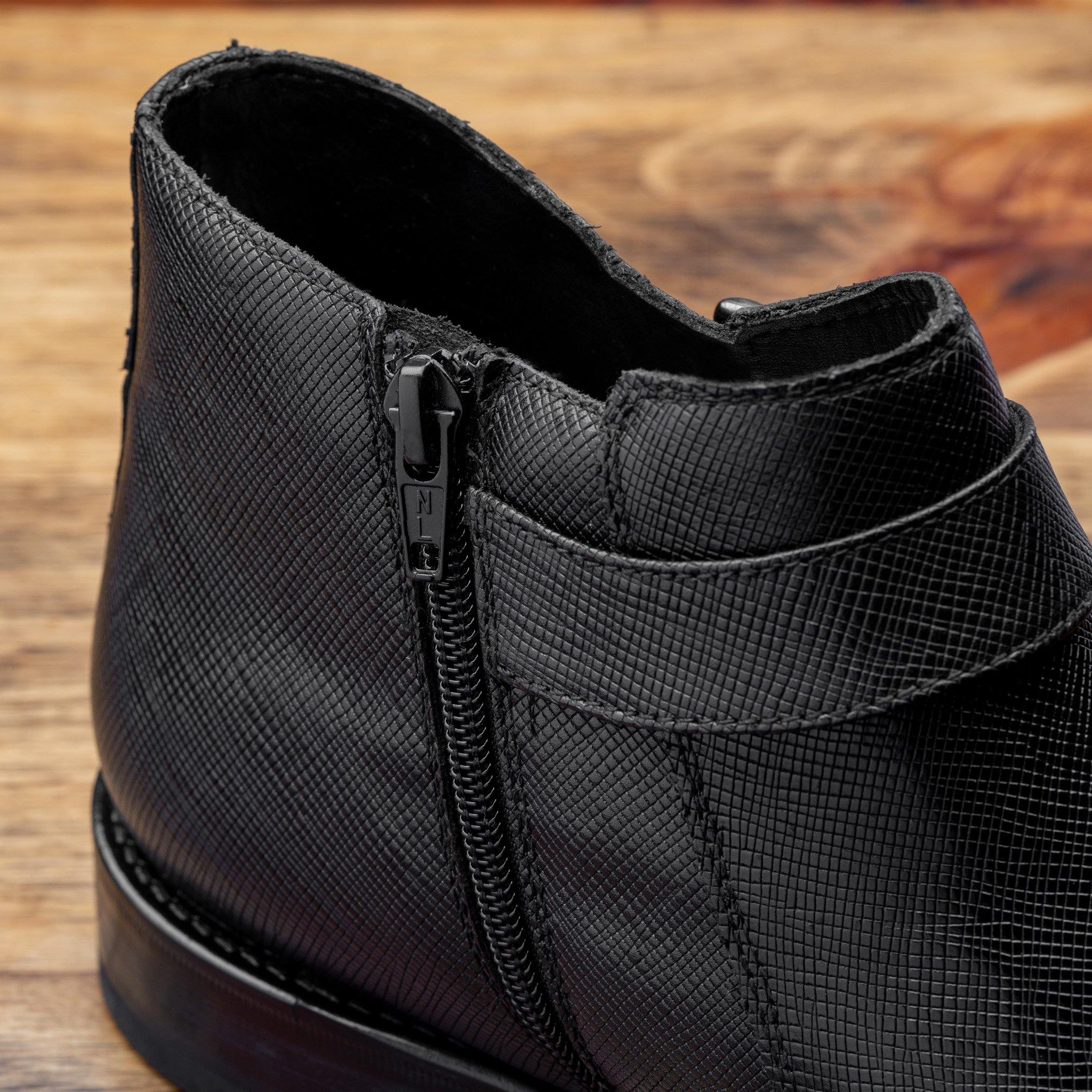 Close-up of Black leather boot on a wooden surface with a gray background