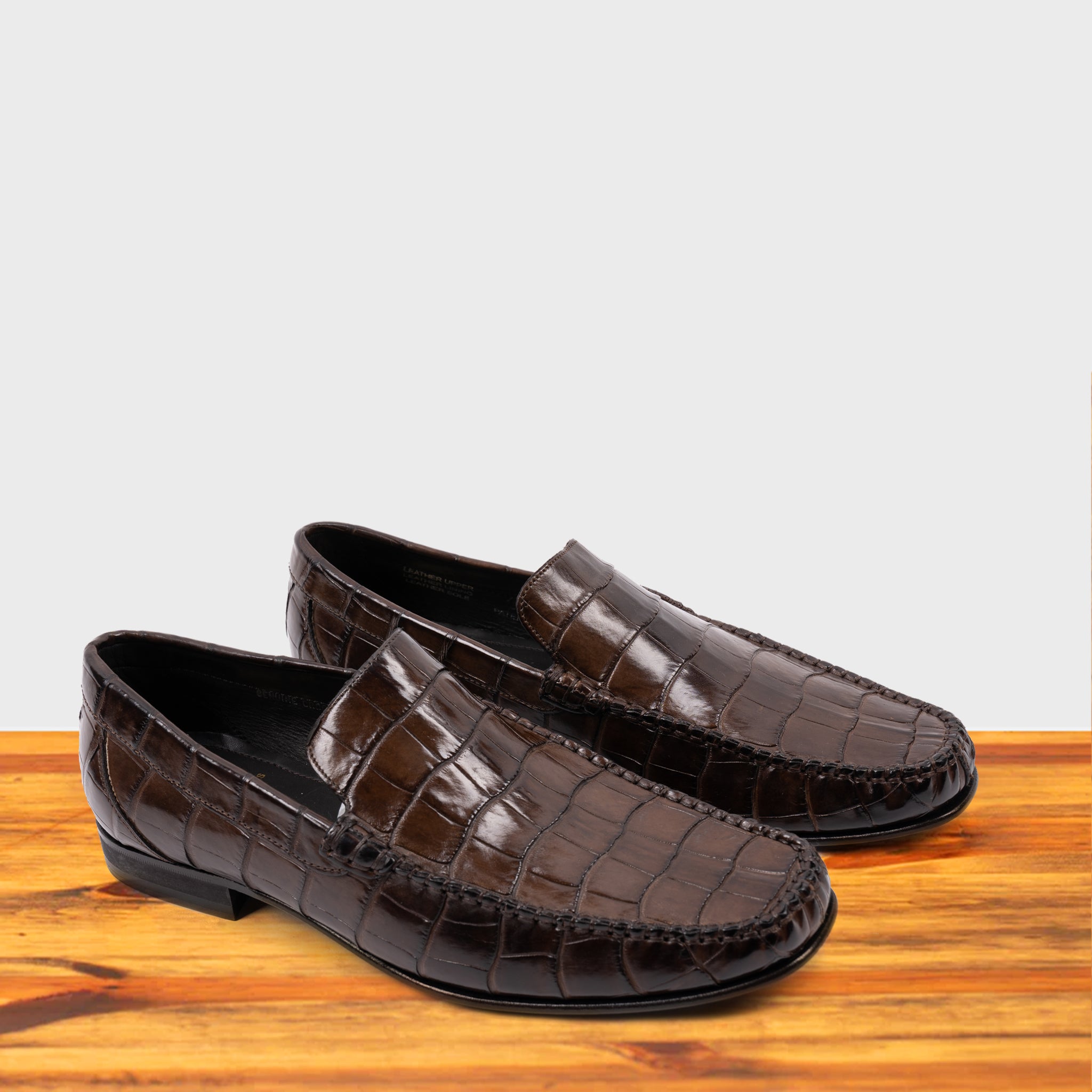 A Pair of Moor crocodile-patterned loafer on a wooden surface with a light gray background