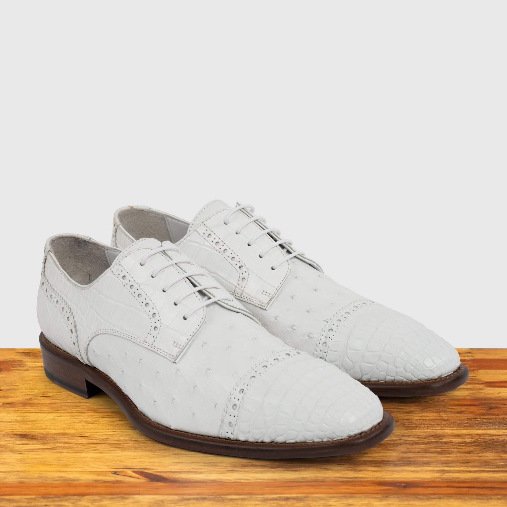 A Pair of white ostrich dress shoe with studded details on a wooden surface