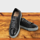 A Pair of Black woven sneaker on a wooden surface with a light gray background