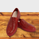 A Pair of Red woven slip-on shoe on a wooden surface with a white background