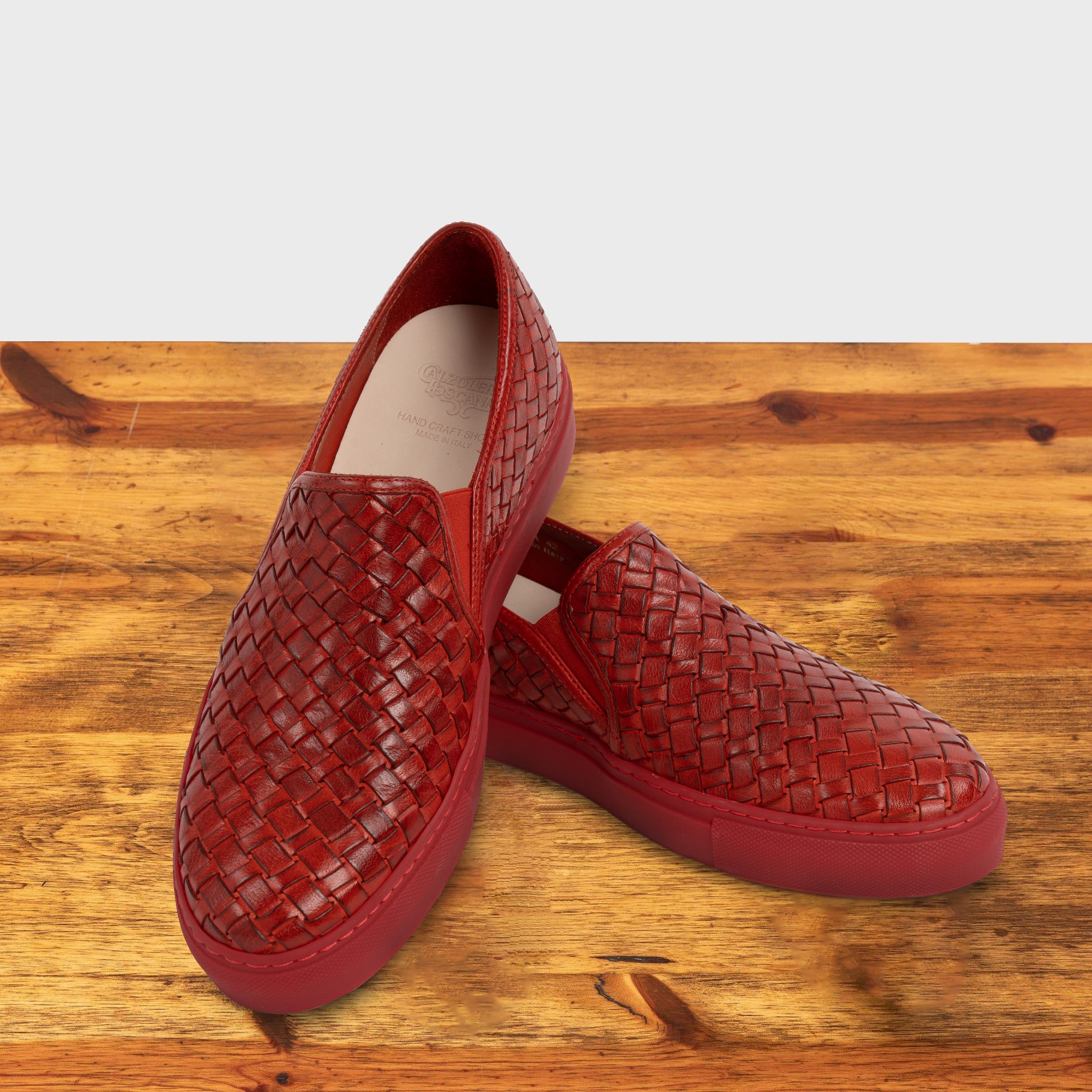 A Pair of Red woven slip-on shoe on a wooden surface with a white background