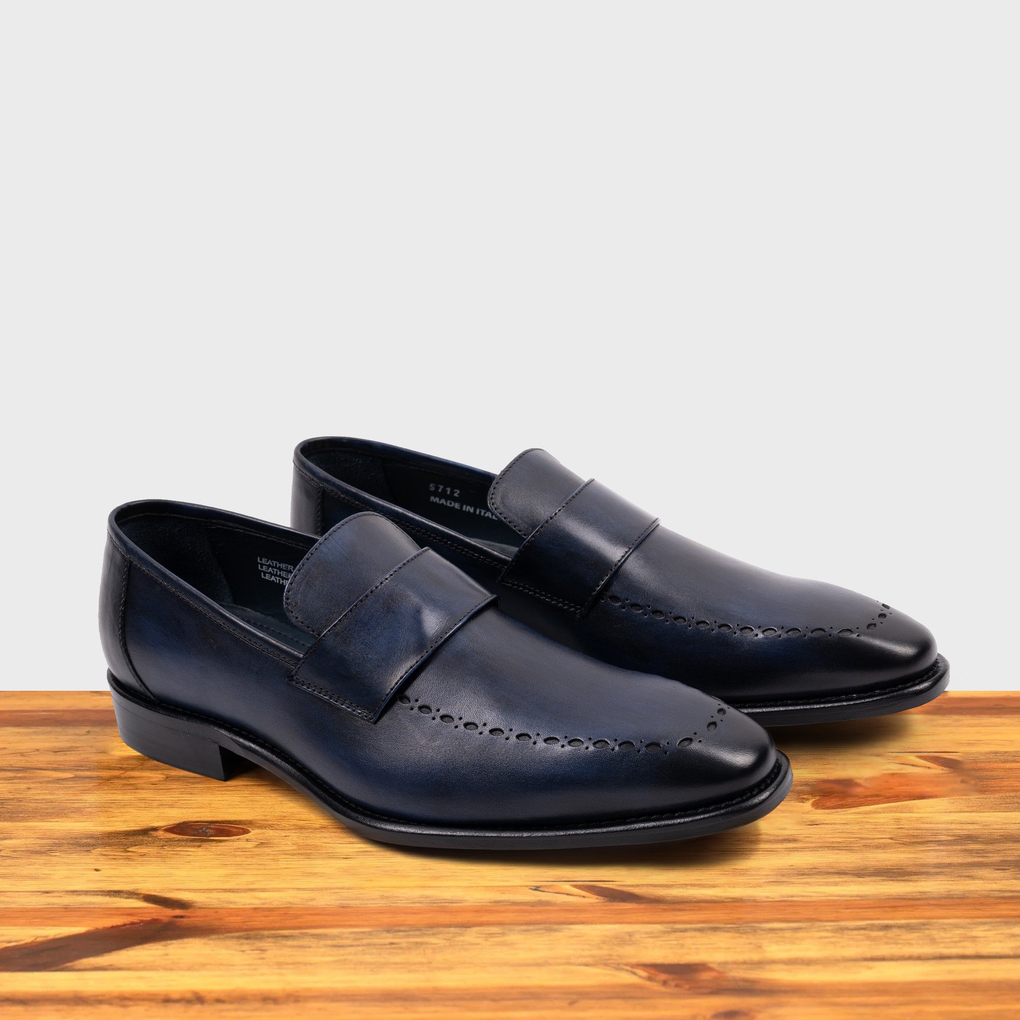Blue leather loafer on a wooden surface with a light gray background
