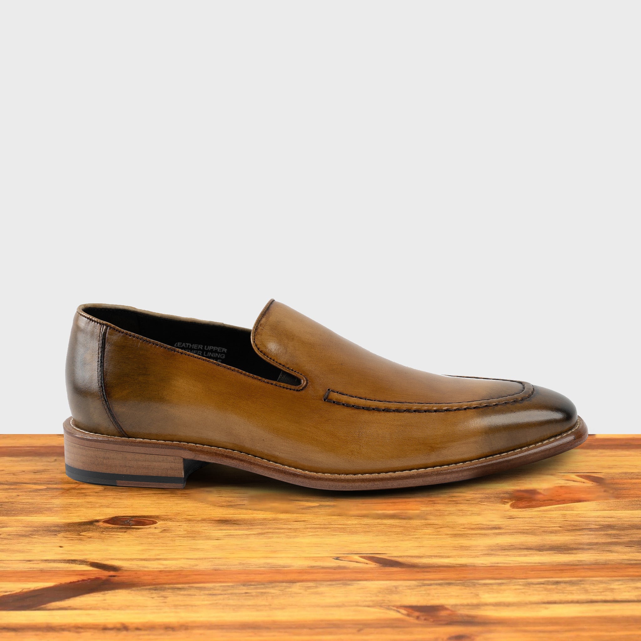 Spice leather loafer on a wooden surface with a light gray background