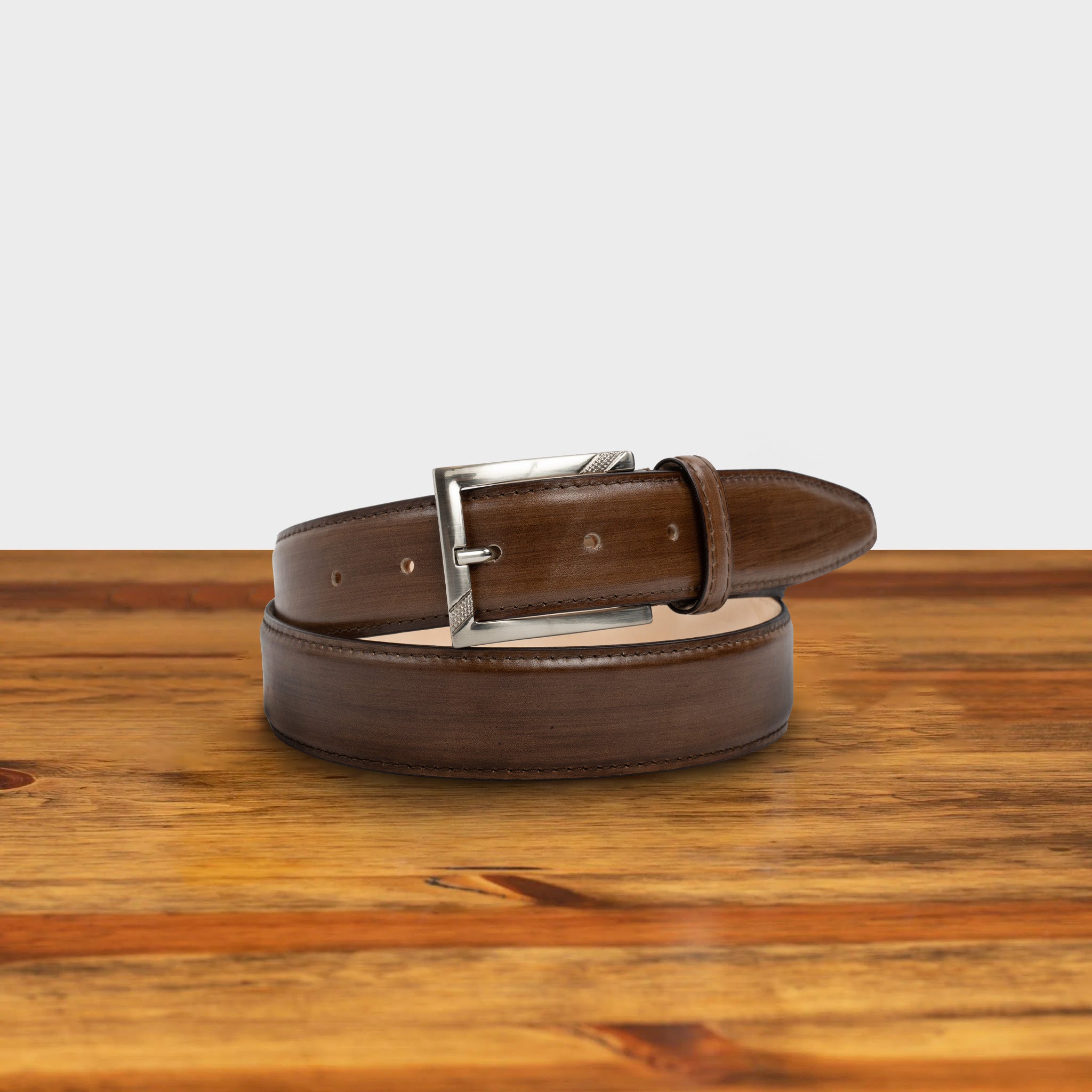 Brown leather belt with a black buckle on a wooden surface