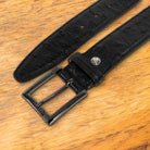 Black ostrich-patterned belt on a wooden surface with a white background