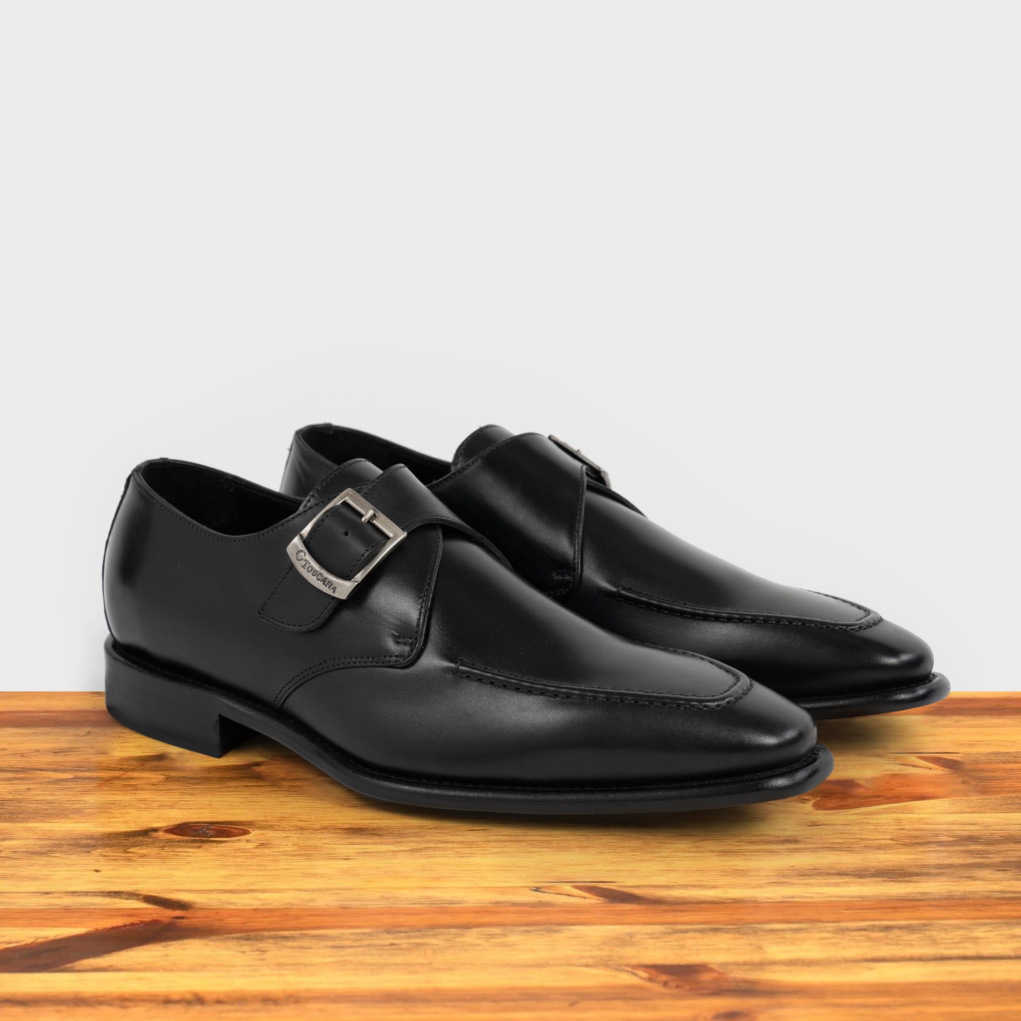 A pair of black monk strap shoe with a silver buckle on a wooden surface