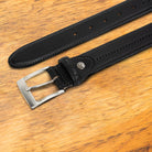 Black leather belt with silver buckle on a wooden surface