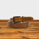 Caramel leather belt on a wooden surface with a light gray background