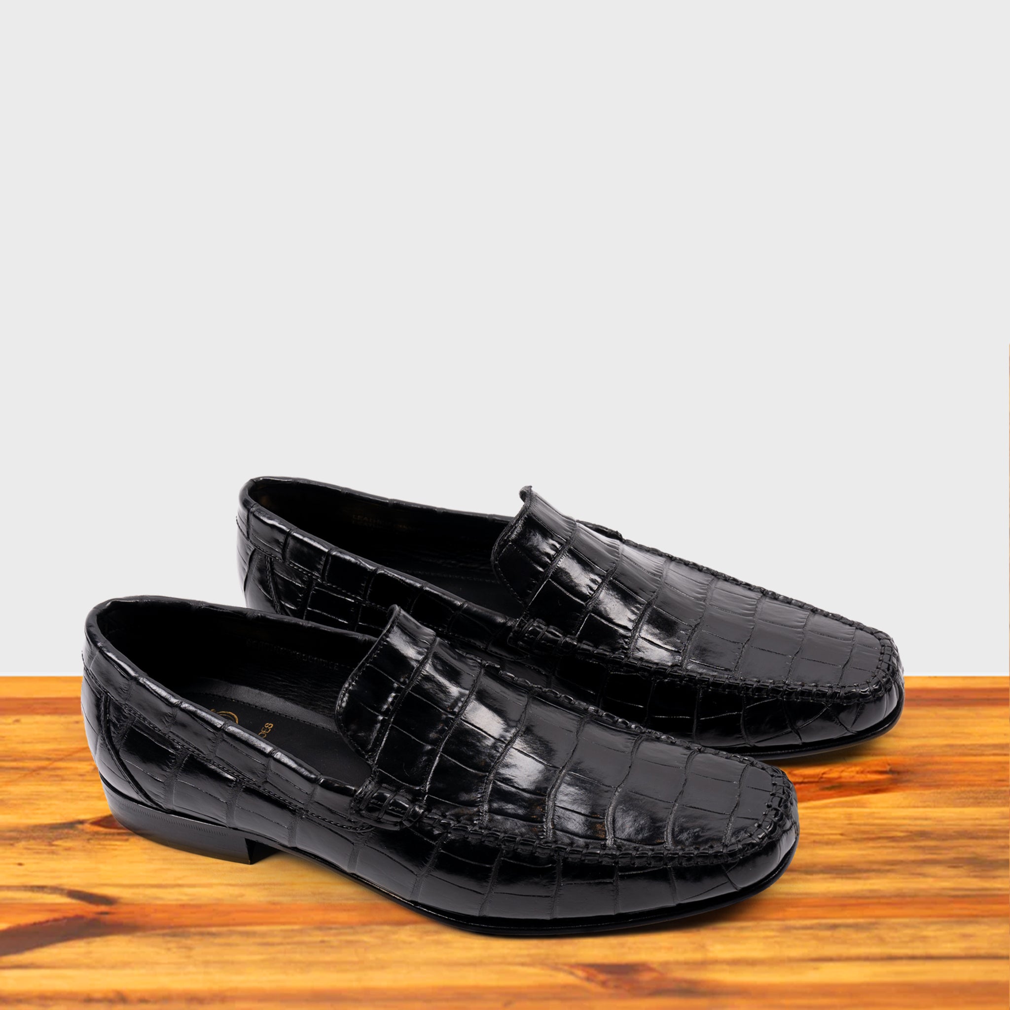 A Pair of Black crocodile-patterned loafer on a wooden surface with a light gray background