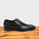 A black monk strap shoe with a silver buckle on a wooden surface