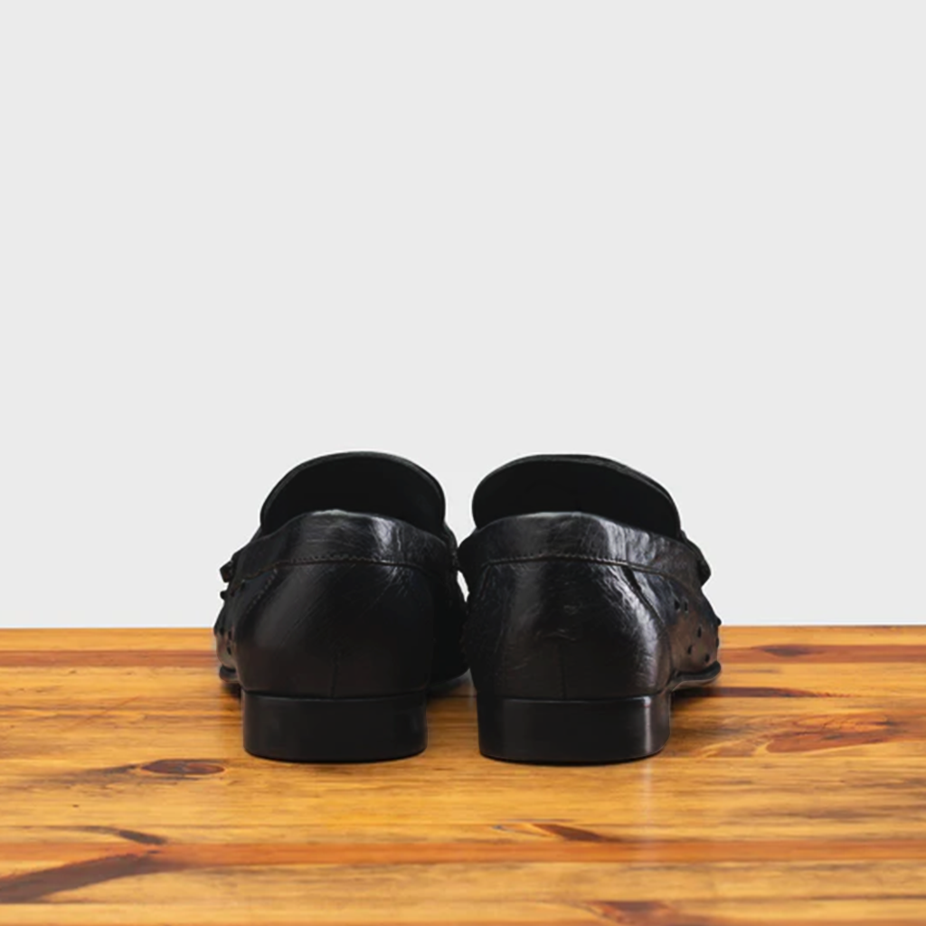 Backside of Black leather loafer on a wooden surface with a light gray background