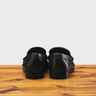 Backside of Black leather loafer on a wooden surface with a light gray background