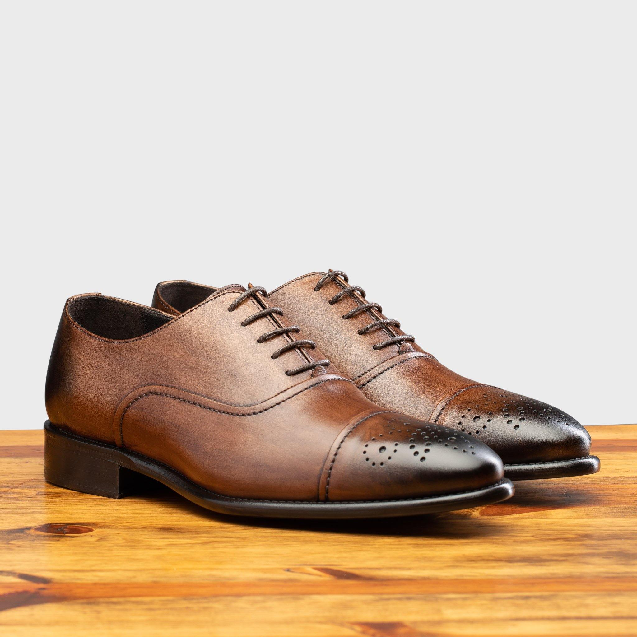 Pair of brown leather oxford dress shoes with a polished finish, placed side by side on a wooden surface