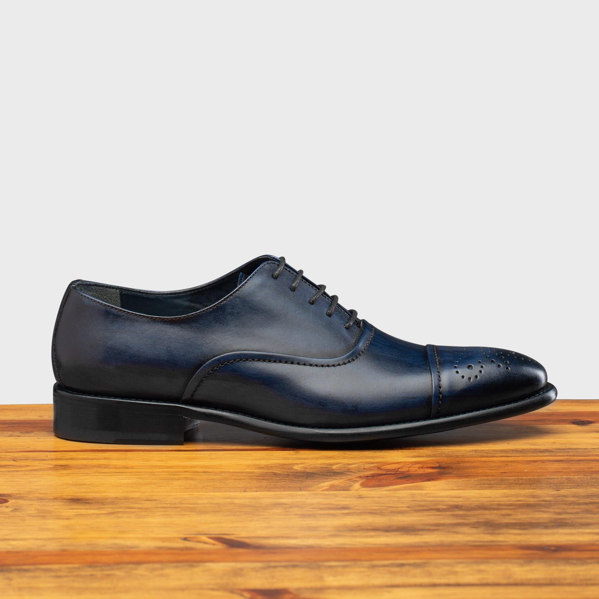 Blue leather dress shoe on a wooden surface with a white background