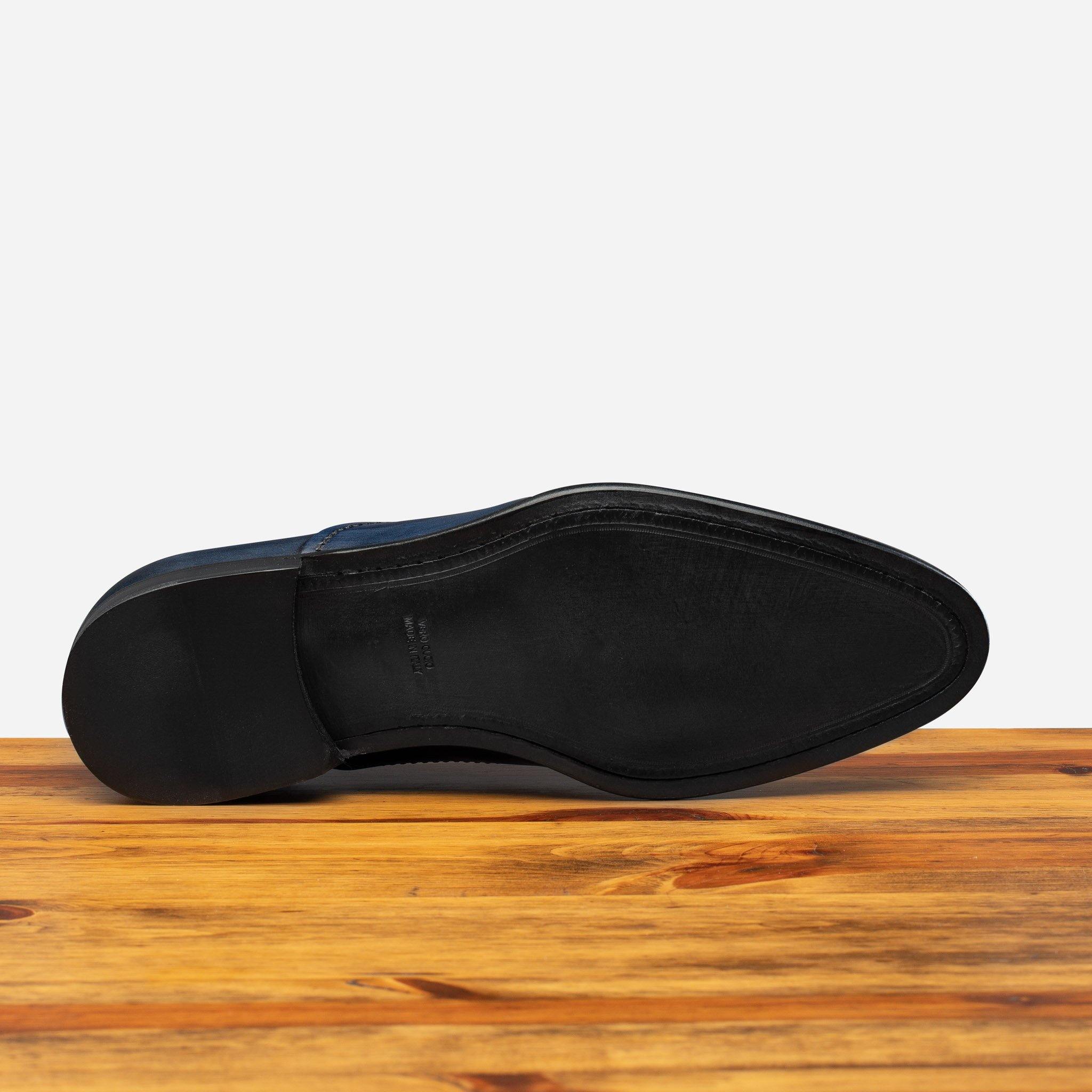 Outsole of Blue leather dress shoe on a wooden surface with a white background