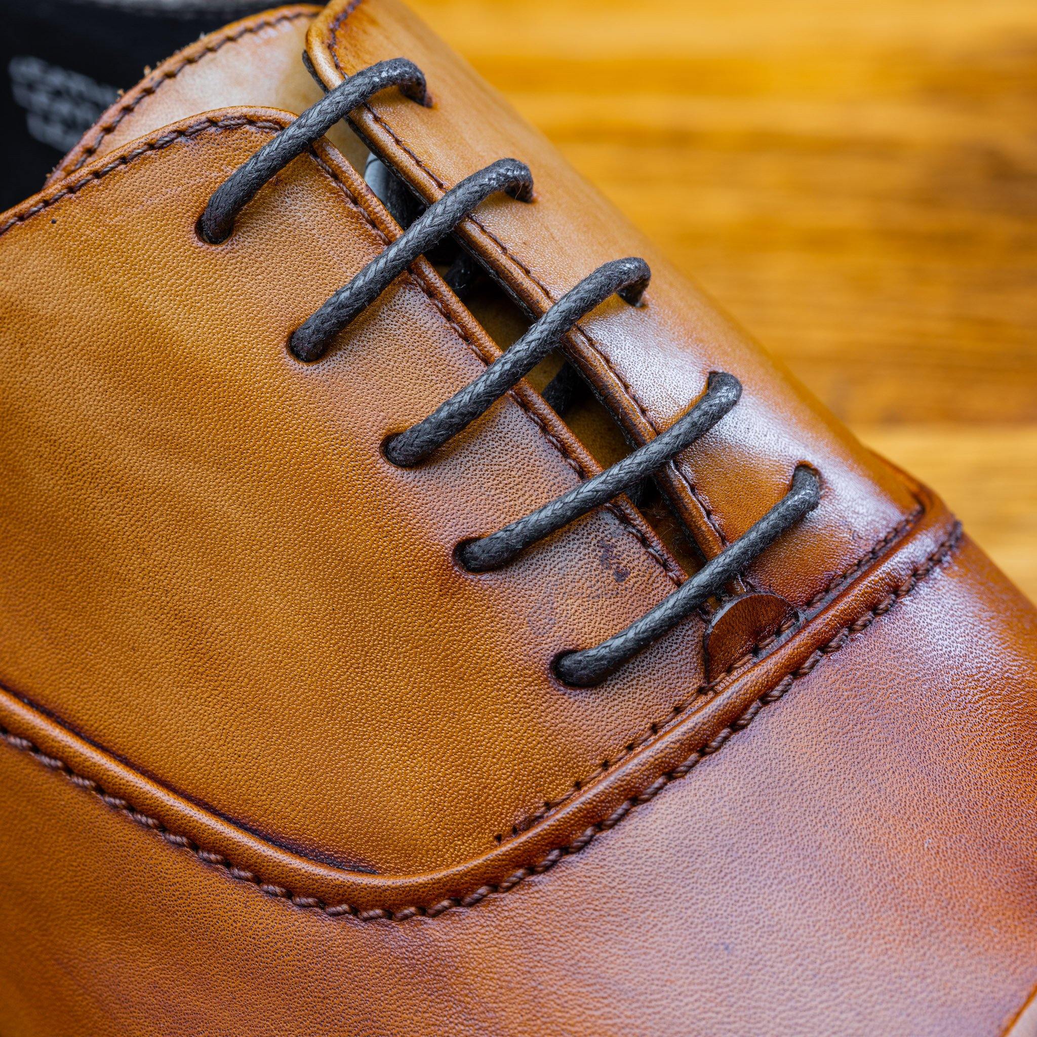Close view of Dark Caramel leather dress shoe on a wooden surface