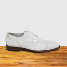A Pair of white ostrich dress shoe with studded details on a wooden surface