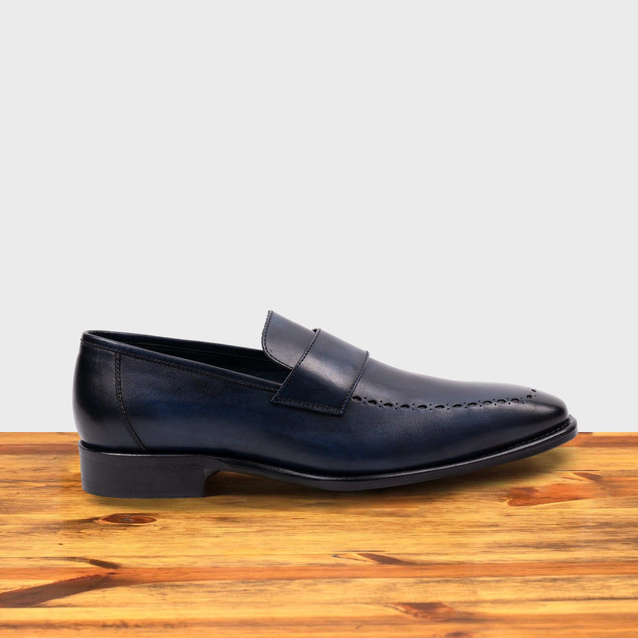 Blue leather loafer on a wooden surface with a light gray background