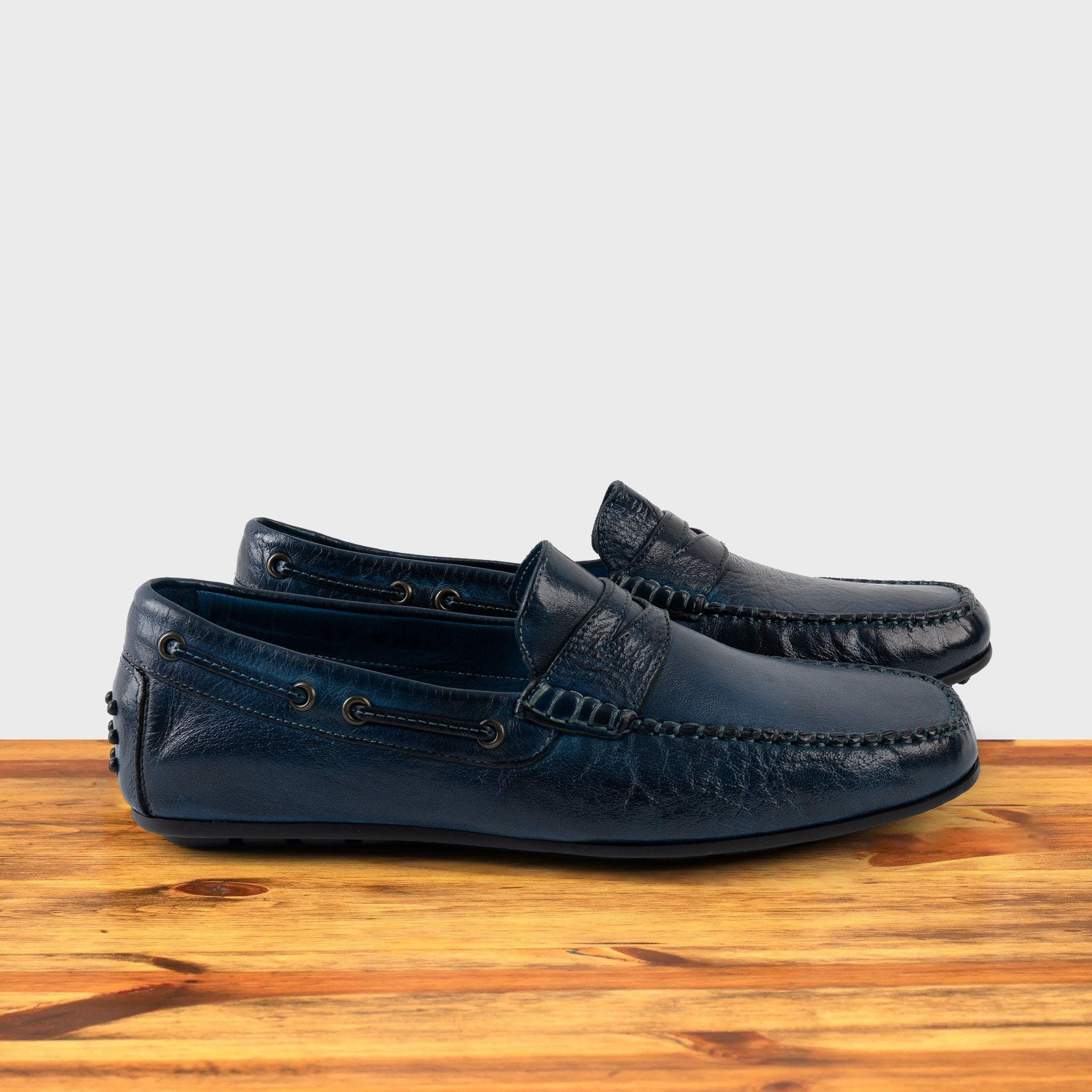 A Pair of Blue leather loafer on a wooden surface with a white background